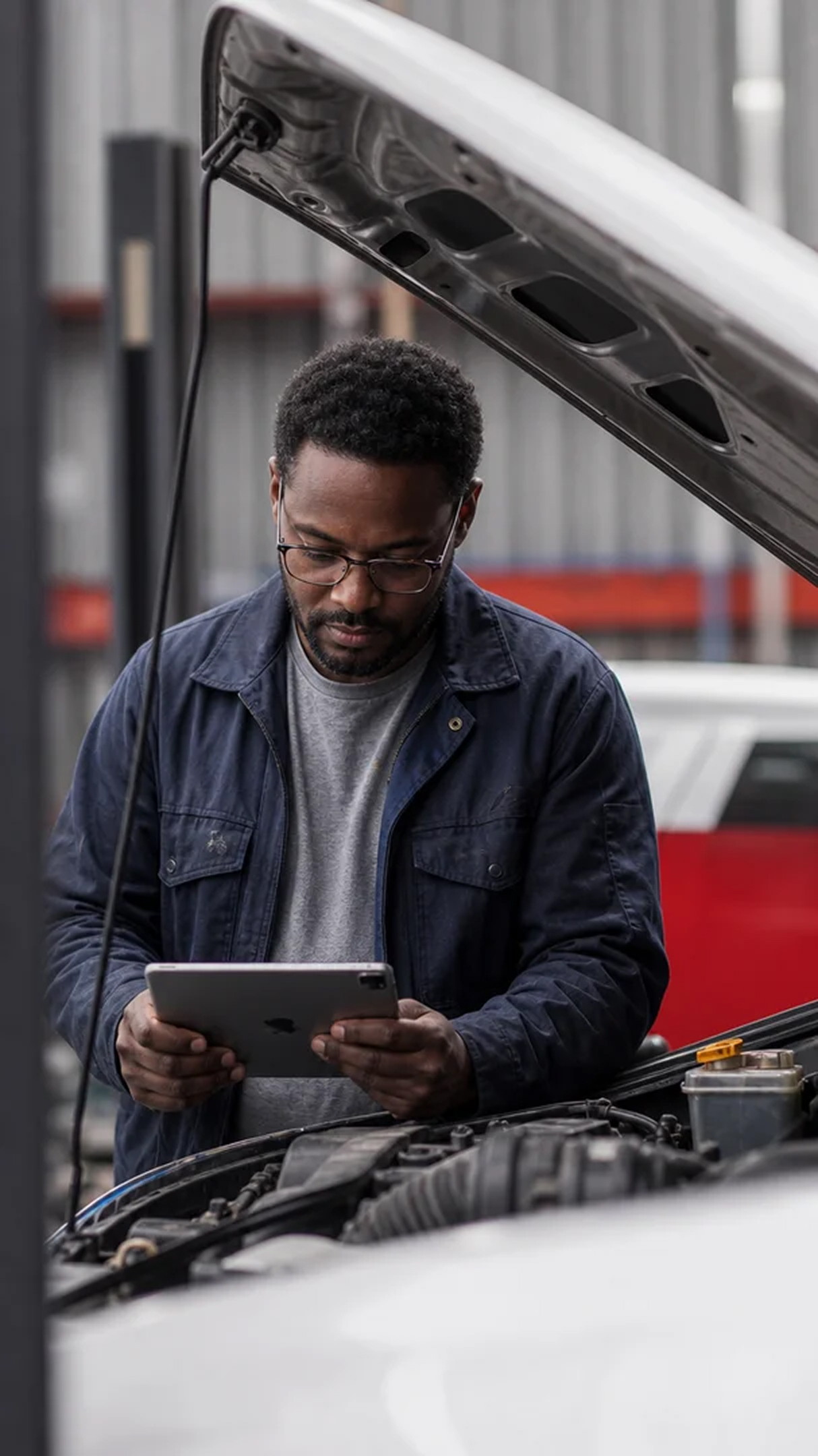 Mechanic standing by an open car bonnet with a tablet.